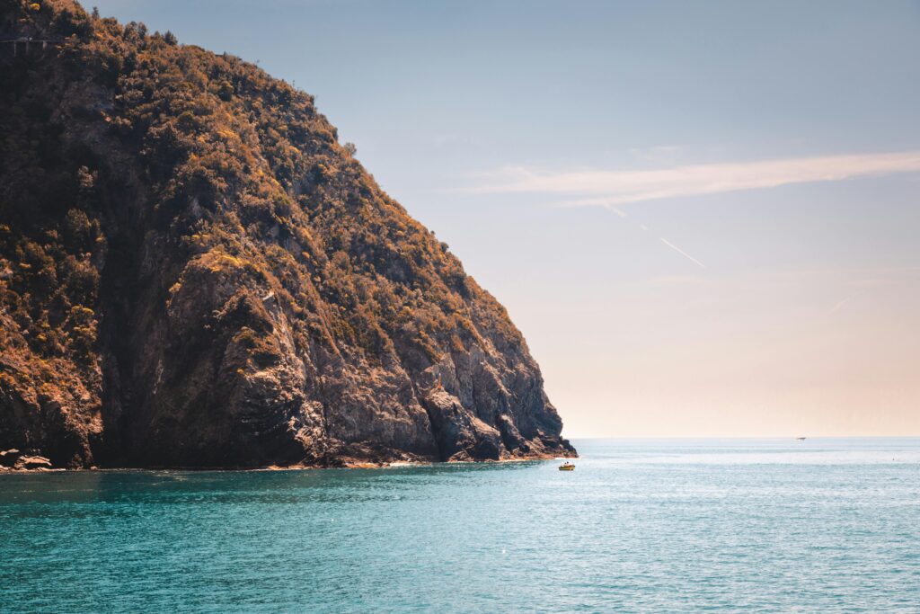 A stunning view of a rocky coastline and calm sea in Liguria, Italy under a clear sky.